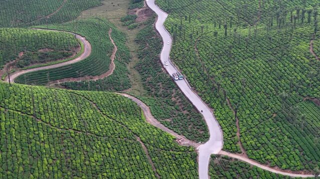 Wide cinematic aerial of Valparai highlighting intersecting hillside roads, expansive tea gardens, and textured green slopes, creating a visually rich and tranquil natural landscape.