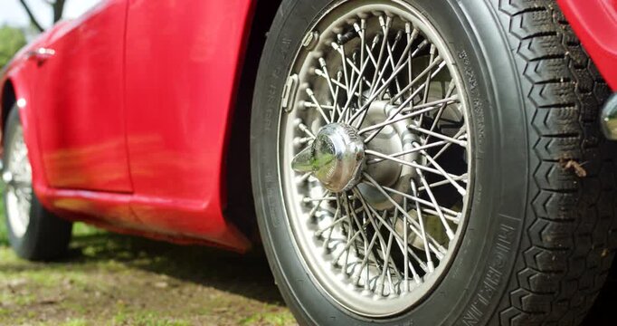 Close up of a classic wire spoke wheel and chrome hubcap on a red vintage car in outdoor sunlight