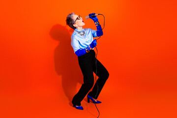 Obraz premium Energetic retro glam singer performs with microphone against a bright orange backdrop