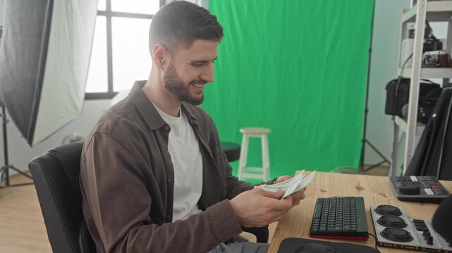 Man counting dollars with hands at studio desk with green screen and camera gear visible; satisfaction and focus.