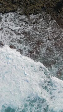 Aerial view of rocky, volcanic shoreline and foamy ocean waves flooding the seaside coast, Tenerife, Canary Islands, Spain