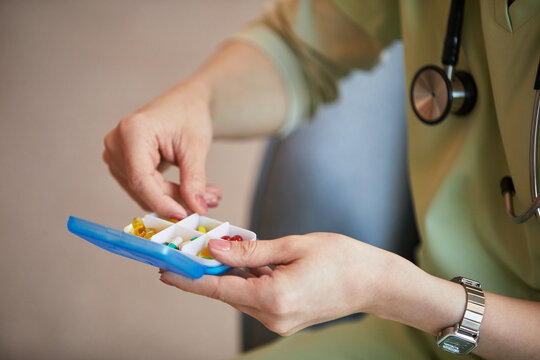 Close up of middle aged female nurse sorting pills in medication organizer at nursing home, supporting senior care and treatment adherence
