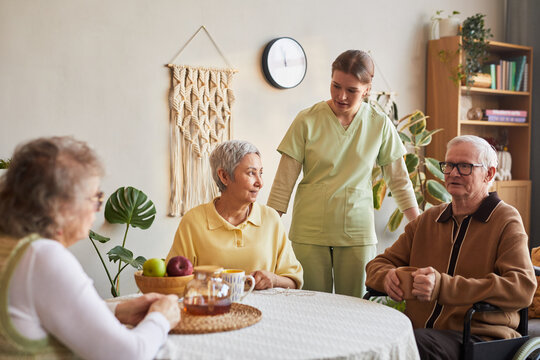 Senior caregiver assisting elderly residents during tea time in nursing home, supporting daily care and social interaction