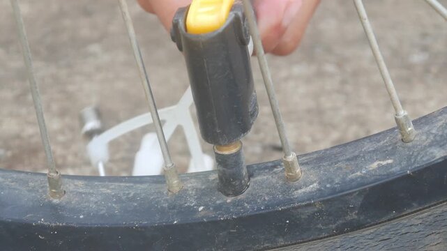 A person is pumping up a bicycle tire using a manual hand pump outdoors.
