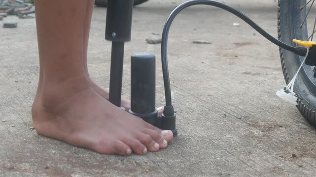 A man's feet holding the base of a manual hand pump while pumping up a bicycle tire outdoors