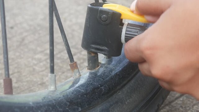 A person is pumping up a bicycle tire using a manual hand pump outdoors.