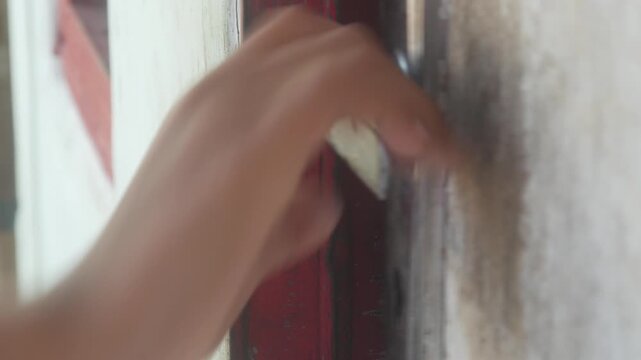 A person's hand is holding or trying to open a wooden door handle.