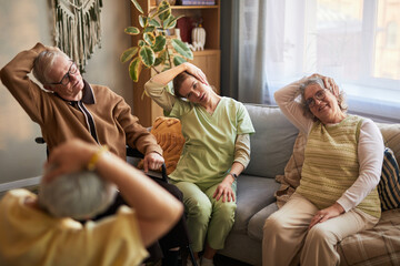 Senior men and women with female caregiver stretching necks during group exercise in nursing home,...
