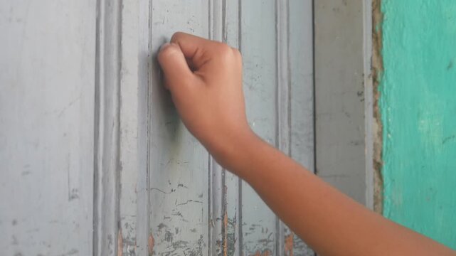 Someone's hand was knocking on the old gray wooden door with a fist