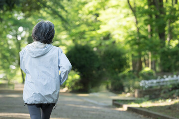Obraz premium 新緑の公園で運動するアクティブシニア女性の見上げる笑顔健康維持のスポーツでウォーキングやランニングのイメージ 顔無しの後ろ姿でコピースペースあり