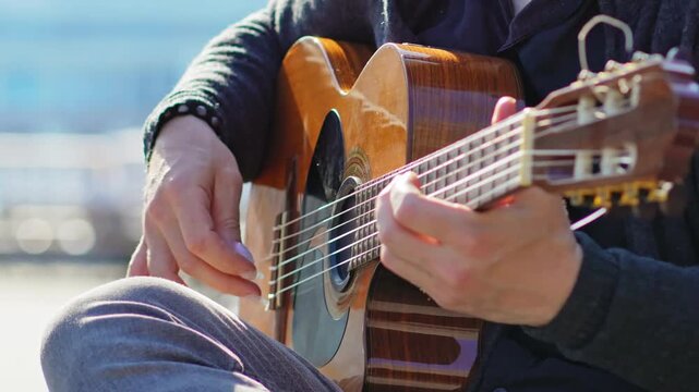 Guitar Player Hands Playing Acoustic Guitar.Slow motion footage of hands playing an acoustic guitar. Close-up of fingers on strings and fretboard. Relaxing music, sunny outdoor lighting, music product
