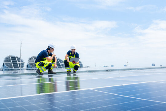 Engineers working on solar panels with laptop on rooftop, renewable energy system installation and maintenance, technicians analyzing photovoltaic data, sustainable energy clean power technology.