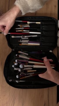 Female artist organizing paint brushes in a black case on wooden table