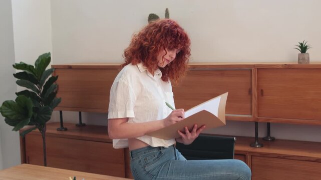 Young redhead woman writing documents at work