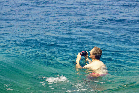 Man in turquoise sea water holding snorkeling mask close to face. Portrays readiness for underwater exploration, preparation phase before immersion, and intentional transition into aquatic environment