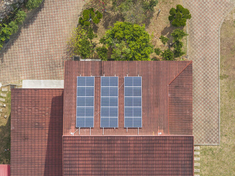 Aerial view of solar panels installed on a red-tiled roof with checkered paved walkways and green trees in Taiwan.