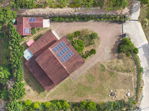 Aerial view of a residential house with solar panels on a red roof surrounded by a paved driveway and green trees in Taiwan.