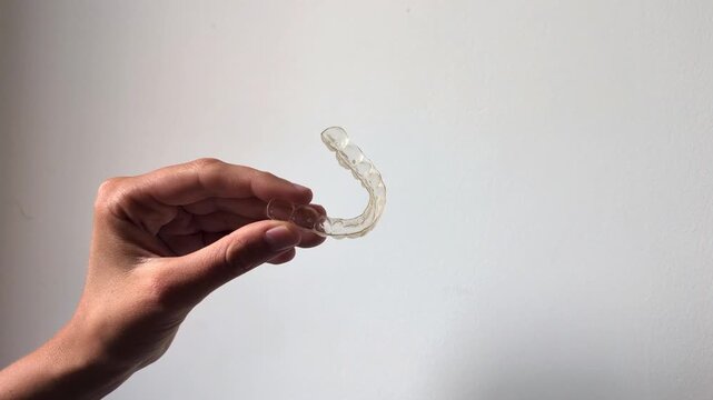 Hand holding transparent dental aligner on white background, orthodontic teeth straightening concept, invisible braces close-up, oral healthcare.