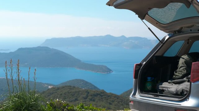 Road trip car overlooking a scenic ocean viewpoint. Station wagon car parked at a scenic viewpoint with its trunk open, revealing camping gear and a breathtaking view of the sea, islands, mountains