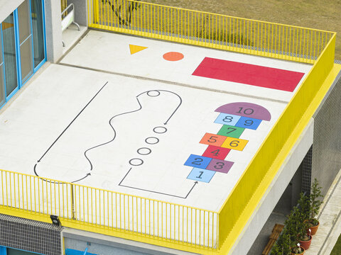 Aerial view of a colorful rooftop playground with a hopscotch grid, geometric shapes, a winding path, and a yellow railing in Taiwan.