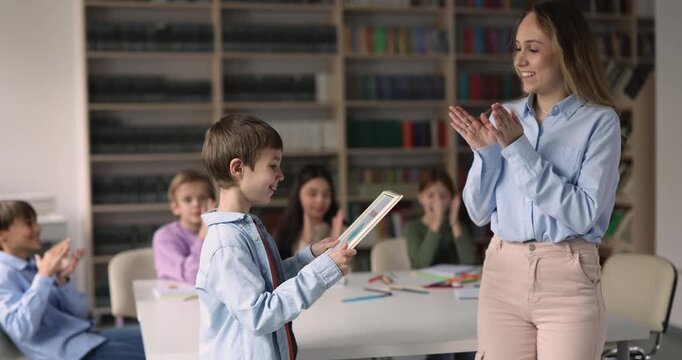 Teacher congratulating schoolboy receiving diploma or certificate, celebrating academic achievement in classroom. Education success, learning progress reward, student recognition, motivation concept