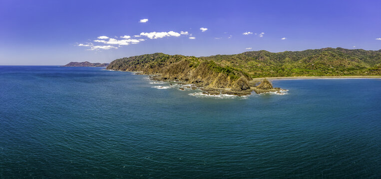 Aerial view of the rugged coastline with rocky cliffs and turquoise waters under a clear blue sky in Cabo San Lucas, Baja California Sur, Mexico.