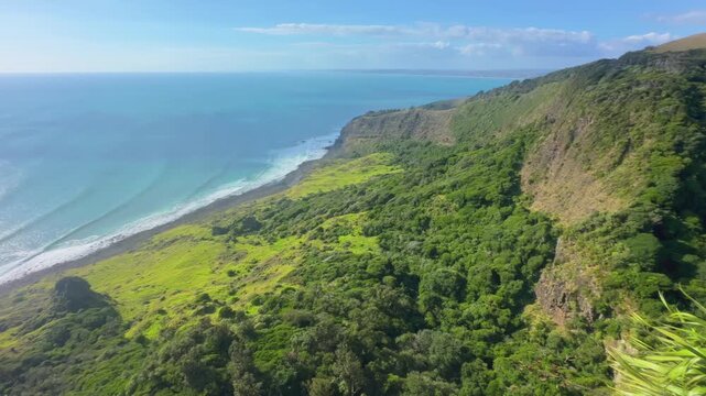 A scenic view of the rugged coastline and lush green hills of the Raglan, Waikato, New Zealand, overlooking the turquoise ocean on a clear day.