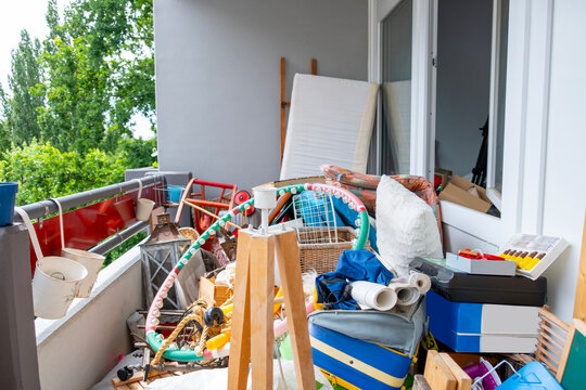 Cluttered balcony filled suitcases, piles clothes household mess creating chaotic cramped living space Psychological tension, Claustrophobic domestic scene with excessive belongings lack organization