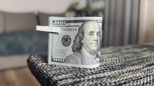 Stack of US hundred dollar bills held by clothespin on textured surface, money laundering or savings concept