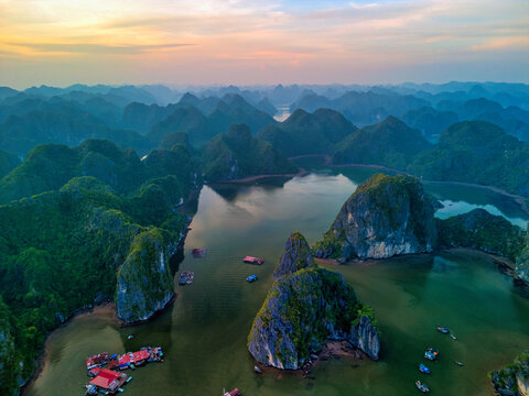 Aerial view of Cat Ba Archipelago limestone karsts rising from the emerald waters with floating fishing villages under a golden sunset sky Ha Tu, Hai Phong, Vietnam.