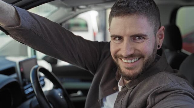 Man holding car keys in an outstretched hand while smiling inside a parked car on a street, showing the keyfob above the steering wheel; friendly welcome.