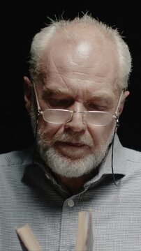 Senior Caucasian man wearing glasses for better vision. Blowing dust from old book. Male clearing pages and opening cover. Reacting to dust with focused look. Standing in dark background in studio.