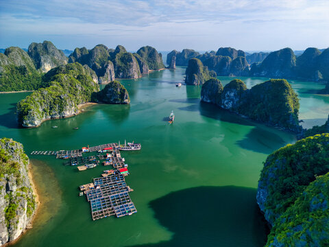 Aerial view of the Cat Ba Archipelago featuring limestone karsts, floating fish farms, and boats on turquoise water in Ha Tu, Hai Phong, Vietnam.
