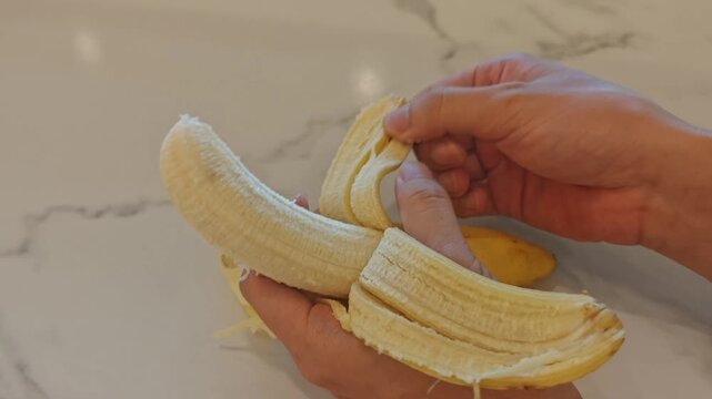 Person Peeling a Ripe Yellow Banana from the Bottom