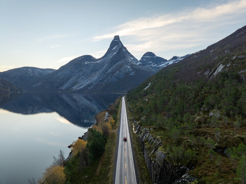 Aerial view of Stetind mountain reflecting in the calm fjord water with a red car driving on the coastal road in Narvik Municipality, Nordland, Norway.