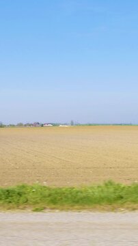 Car side window view of road next to a farm land