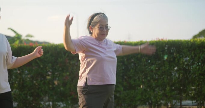 Senior Asian woman doing arm exercises and jumping jacks in the park.