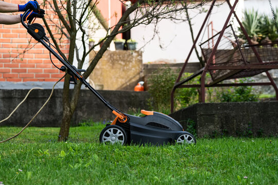 Middle aged woman houseowner mowing the lawn on backyard of his house.