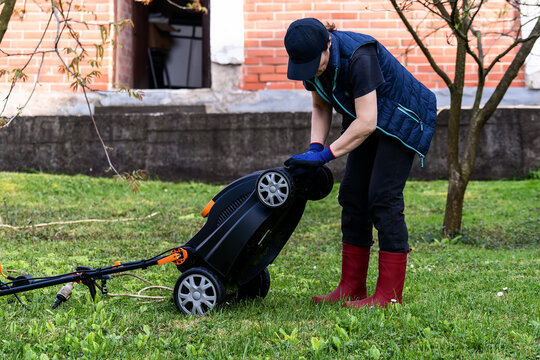 Middle aged woman houseowner mowing the lawn on backyard of his house.
