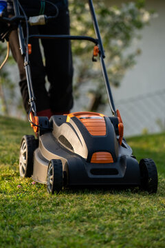 Middle aged woman houseowner mowing the lawn on backyard of his house.