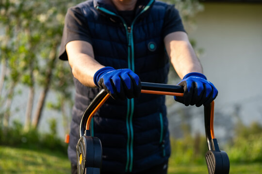 Middle aged woman houseowner mowing the lawn on backyard of his house.