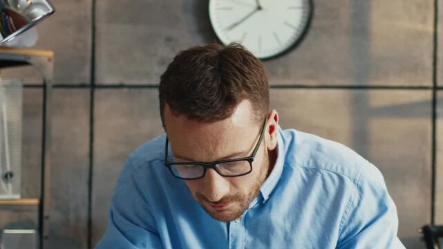 Portrait of Caucasian man wearing glasses while looking at camera. Handsome male sitting still and focusing ahead. Thinking about something. Staying calm in quiet room. Working routine.