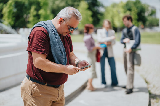 A middle-aged man checks his smartphone while three colleagues chat in the background during a business outing.