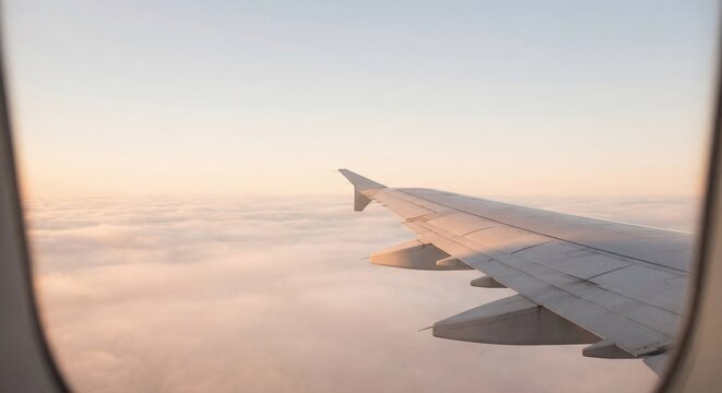 Airplane Wing Above Clouds Through Window at Sunrise