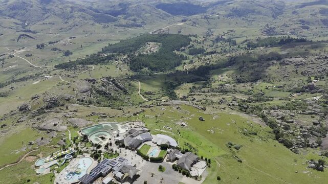 Drone flies backwards high over resort on top of monolith overlooking the valley on a sunny day at Sibebe Rock near Mbabane, Eswatini
