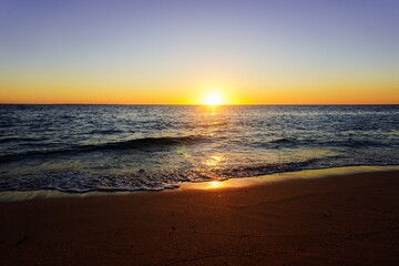 Warm sunset over a calm ocean shoreline with gentle waves and glowing reflections. Ideal for travel, relaxation, and lifestyle themes or background visuals. © Duro Mesiar