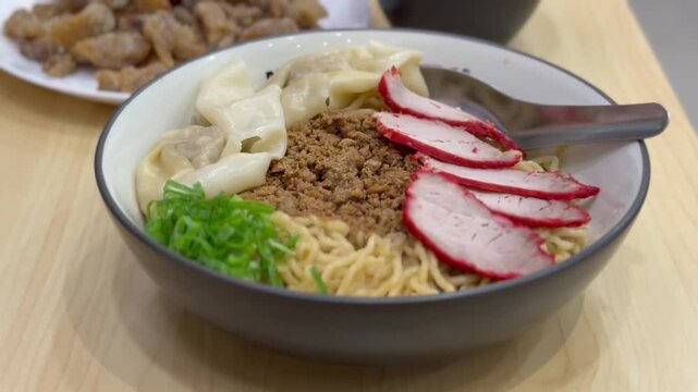 Close up of Indonesian Chinese style pork noodle (bakmi babi) topped with red roasted pork (char siu) and wontons. A savory and comforting dish with rich flavors and textures. 