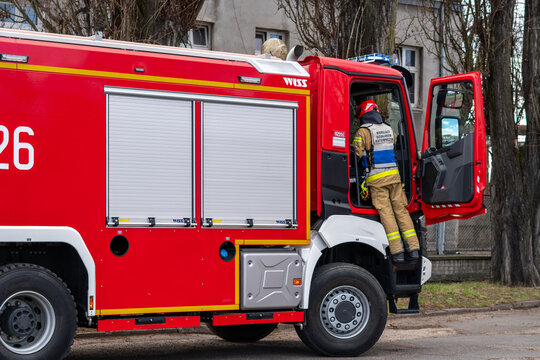 Fire department incident commander by Renault WISS fire truck, firefighter in command vest entering the vehicle cabin, side view of modern red emergency engine, professional rescue services during ope