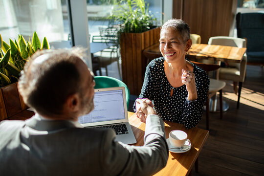 Smiling professionals shake hands in cafe meeting