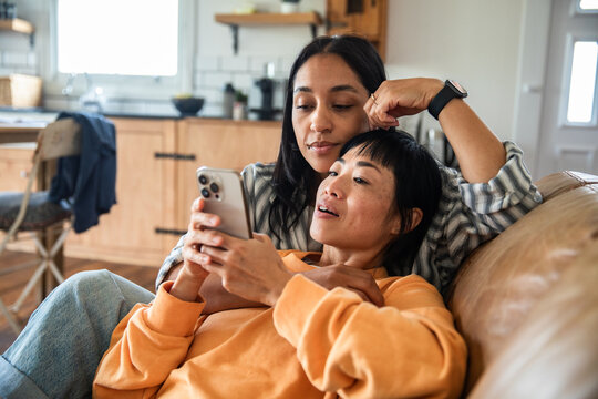 Two women using smartphone on cozy sofa at home
